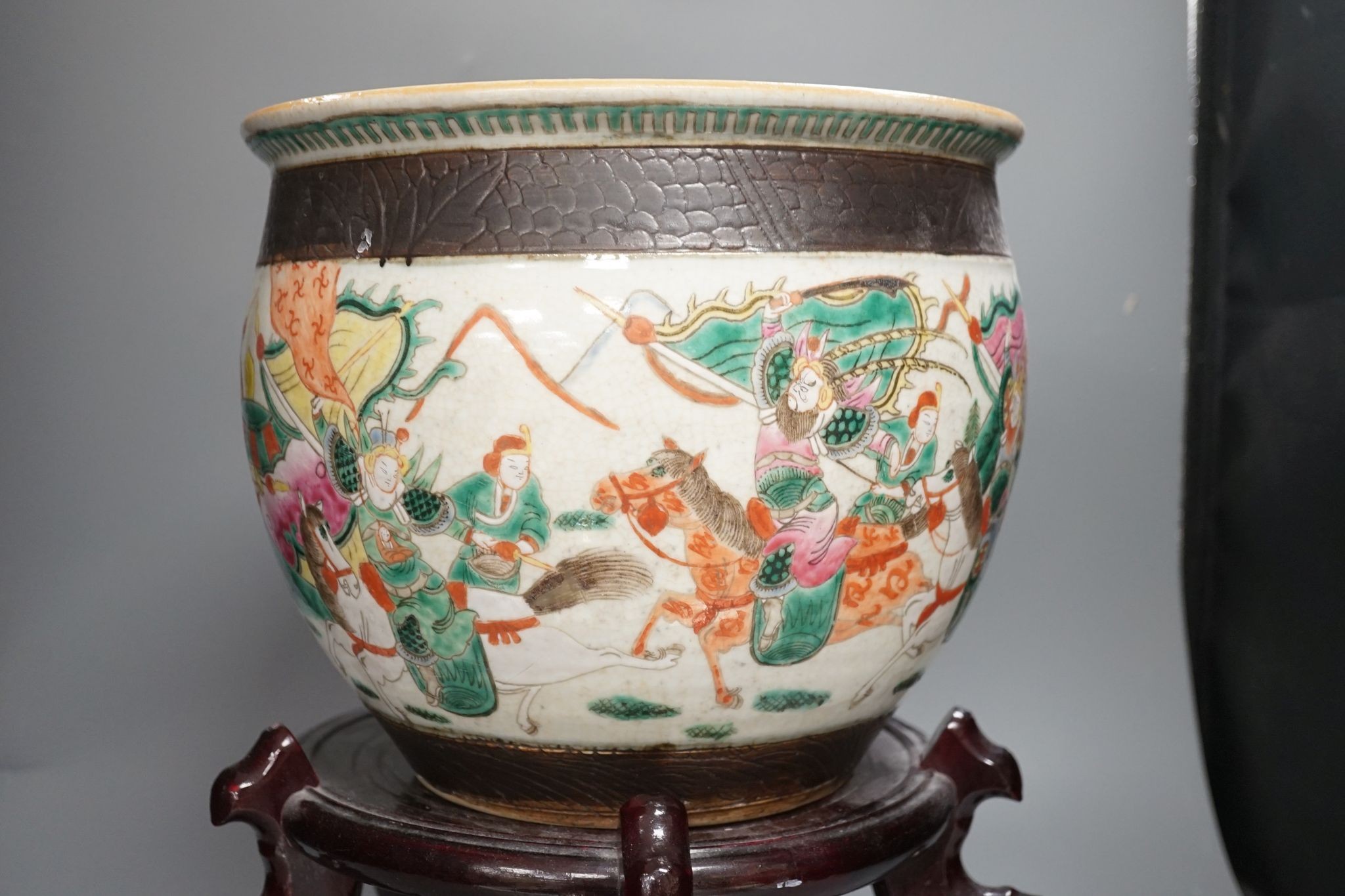 A Chinese famille rose ‘warriors’ jardiniere, late 19th century, wooden stand, 42 cms high including stand.